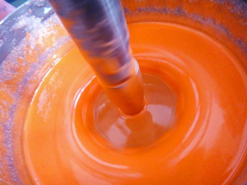 Eine orangefarbene Flüssigkeit wird von einer Maschine gerührt und bildet dadurch einen Ring.