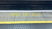 Gelber Schriftzug auf dem Boden einer Bahnstation "Mind the Gap"