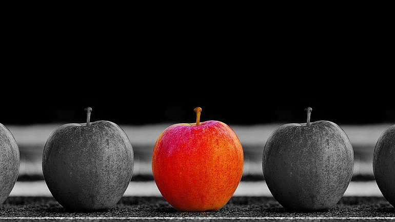 eine Reihe Äpfel in Schwarz-weiß in der Mitte ein roter Apfel 